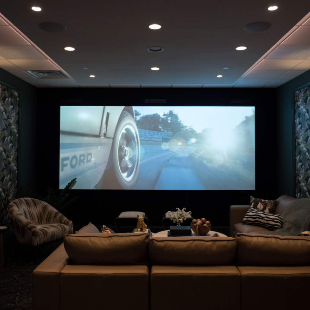 <span class="uk-h4">Overture Lounge home theater with movie playing on large screen, leather sectional and patterned wallpaper</span>