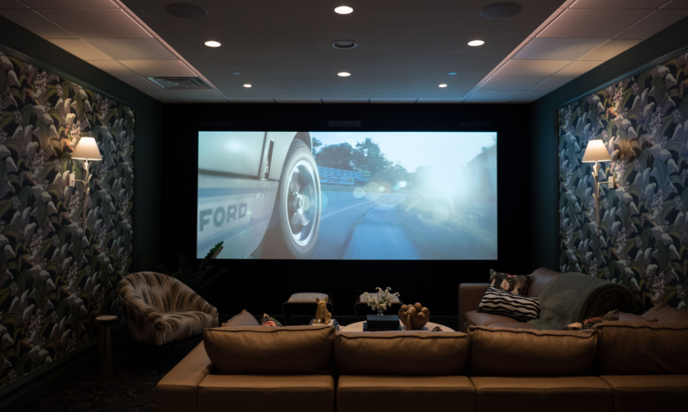 <span class="uk-h4">Overture Lounge home theater with movie playing on large screen, leather sectional and patterned wallpaper</span>